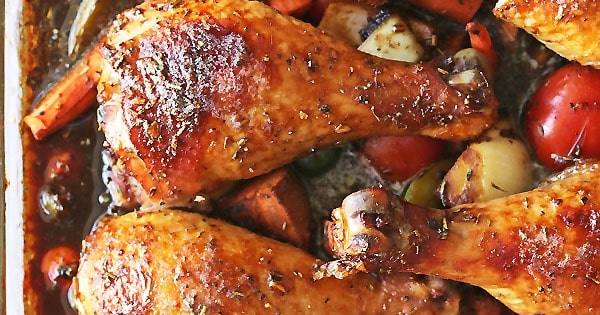 A close-up image of three gooey drumsticks. A bunch of sticky and yummy vegetables are the base of this delicious one pan meal.