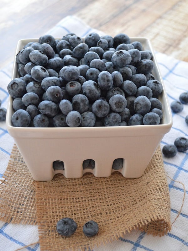 A pint of fresh, plump blueberries spills over onto a blue striped napkin.