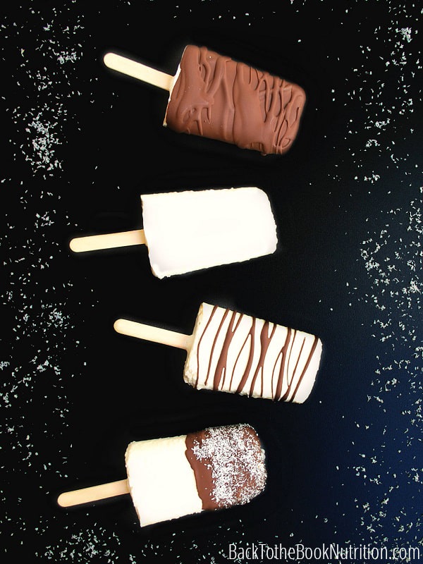 An array of coconut cream popsicles lay on a black background. One is entirely covered in a chocolate shell; one is plain, one features a chocolate swirl, and the fourth is half-dipped in chocolate and covered in powdery coconut flakes. 
