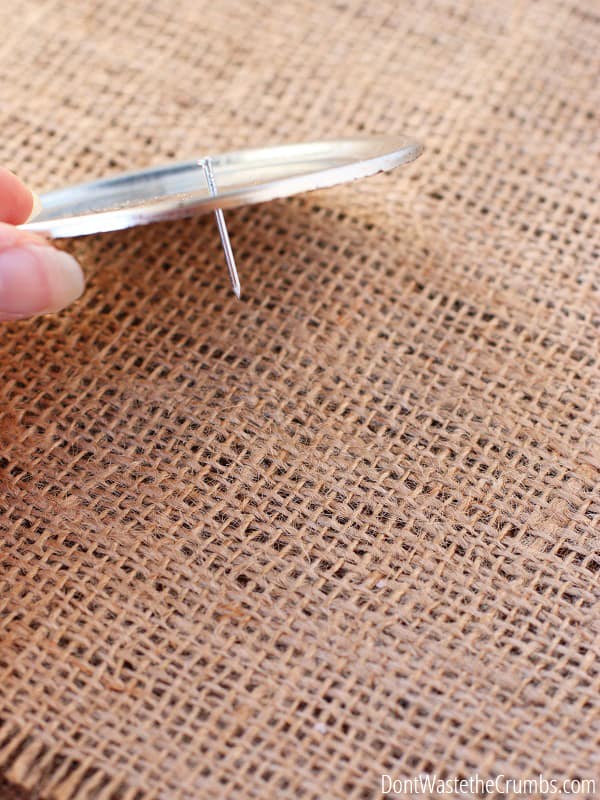 Hand holding mason jar lid with a small nail going through the lid. This will make a flour shaker.