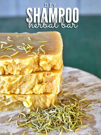 Three shampoo bars stacked up on a counter with herbs sprinkled around. Text overlay says, "DIY Shampoo Herbal Bar".