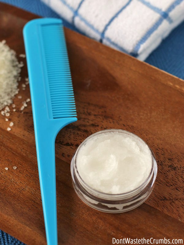 A container of a creamy conditioner with a comb lying nearby, and a folded towel in the background