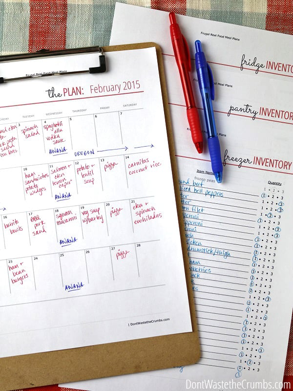 A paper calendar with meals written on in, and freezer, pantry and fridge inventory papers behind it, with two pens on top ready for planning Freezer Cooking Day.