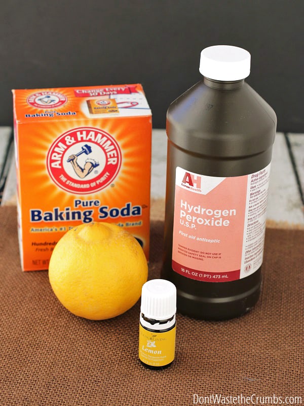 A whole lemon, a box of baking soda, a bottle of hydrogen peroxide, and lemon essential oil sat on a table.