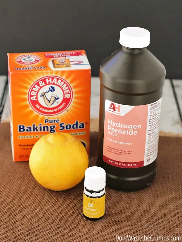A whole lemon, a box of baking soda, a bottle of hydrogen peroxide, and lemon essential oil sat on a table.  
