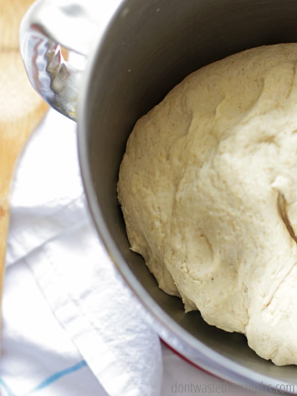 A stand mixer with freshly mixed bread dough, ready to be covered with a towel for rising. 