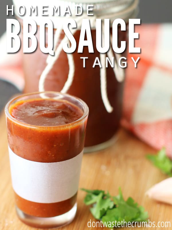 BBQ sauce in a glass with a large mason jar full of BBQ sauce in the background. Text overlay reads, "Homemade BBQ Sauce Tangy".