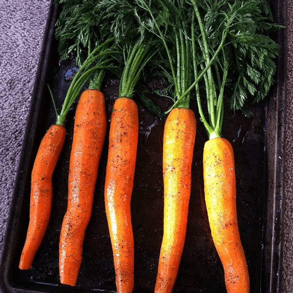 Five beautifully roasted carrots on a cookie sheet.