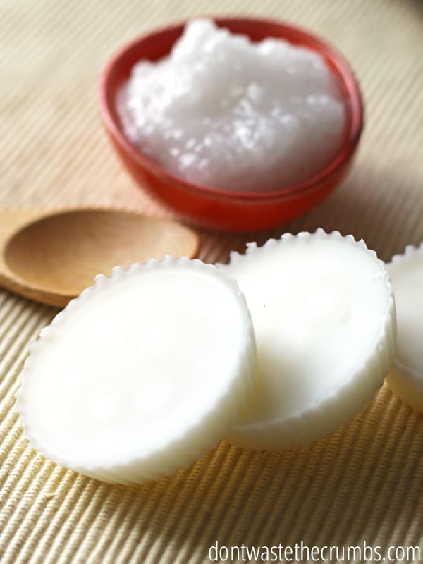 This DIY All-Natural Face Lotion Bar has only two ingredients plus your own added scent. A wooden spoon is set next to a small red bowl filled with smooth and warm lotion is set behind three already completed and formed lotion bars.
