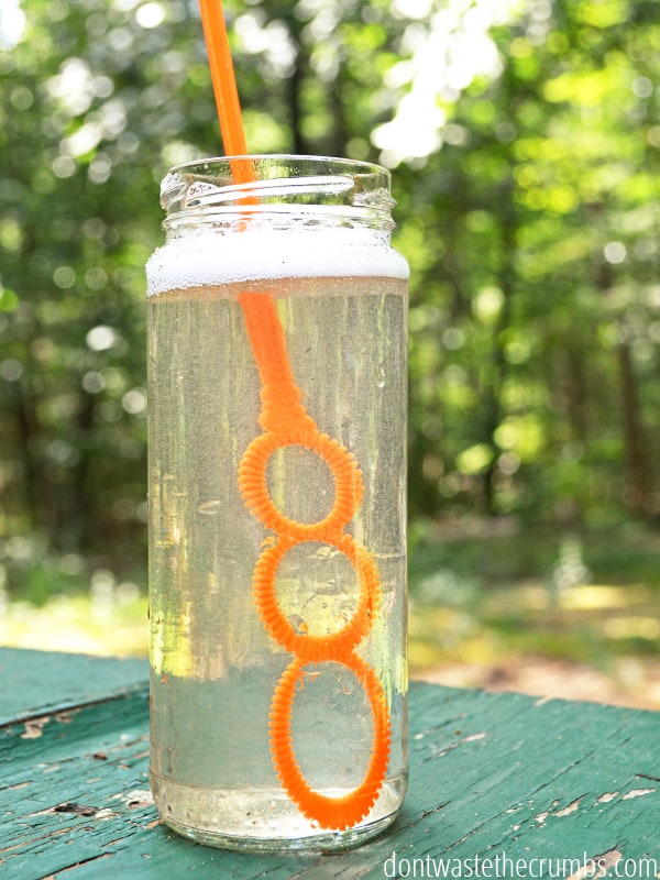 Bottle of homemade bubbles with a bubble wand in it. Photo taken outside in the woods.