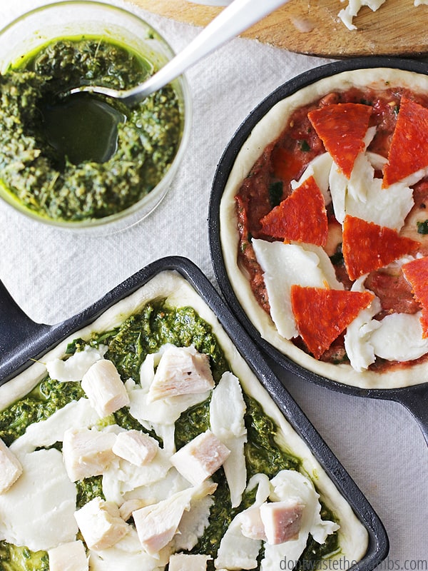 There are two cast iron skillet. One square shape has carrot pesto and chicken as a topping and the other circle skillet pizza is topped with pepperoni and chicken. There is a bowl next to the pizzas that have carrot top pesto and a spoon. The topping ideas are endless!