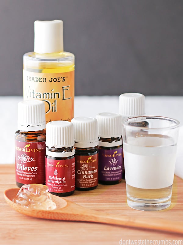 Five bottles of essential oils with a tall bottle of Vitamin E oil beside a wooden spoon filled with glycerin.