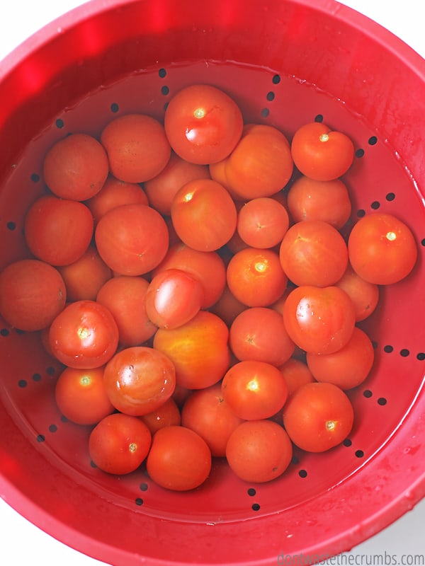 Roma tomatoes in water bath in a red strainer