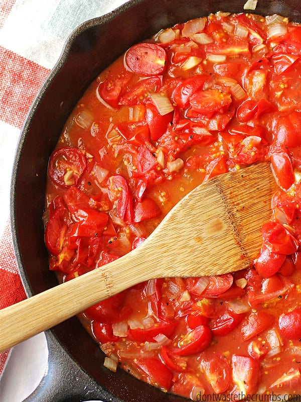 Homemade fresh tomato sauce in a cast iron skillet with a wooden spoon stirring.