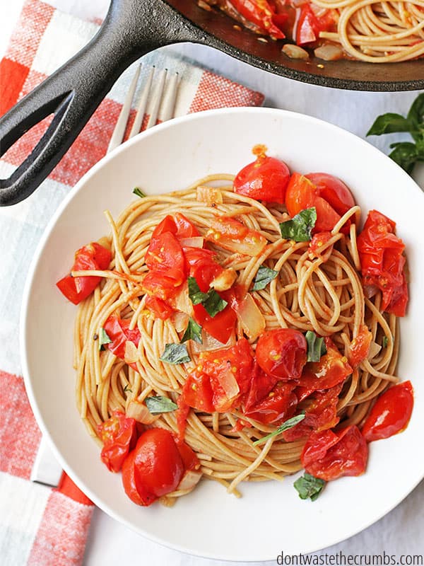 A white plate with spaghetti and fresh tomato sauce. Sliced tomatoes are sprinkled throughout.