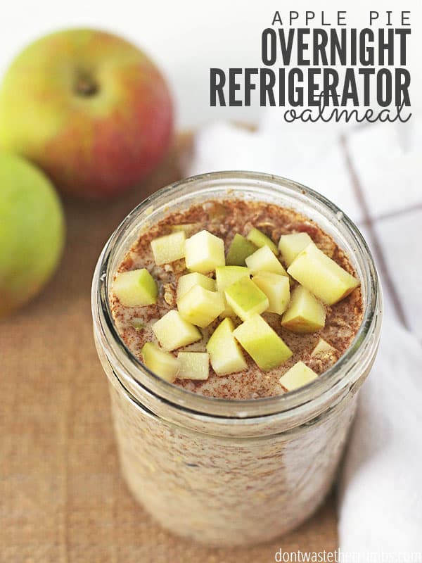 Jar of overnight oatmeal topped with chopped apples sitting on a cutting board with apples in the background. Text overlay says, "Apple Pie Overnight Refrigerated Oatmeal".