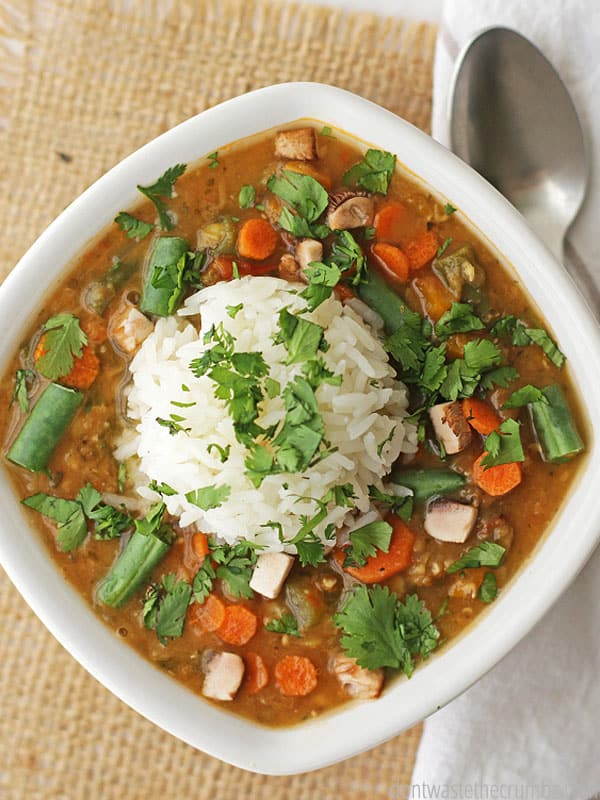 Red lentil vegetable soup with a scoop of white rice on top. Cilantro sprinkled throughout. This is in a white bowl.