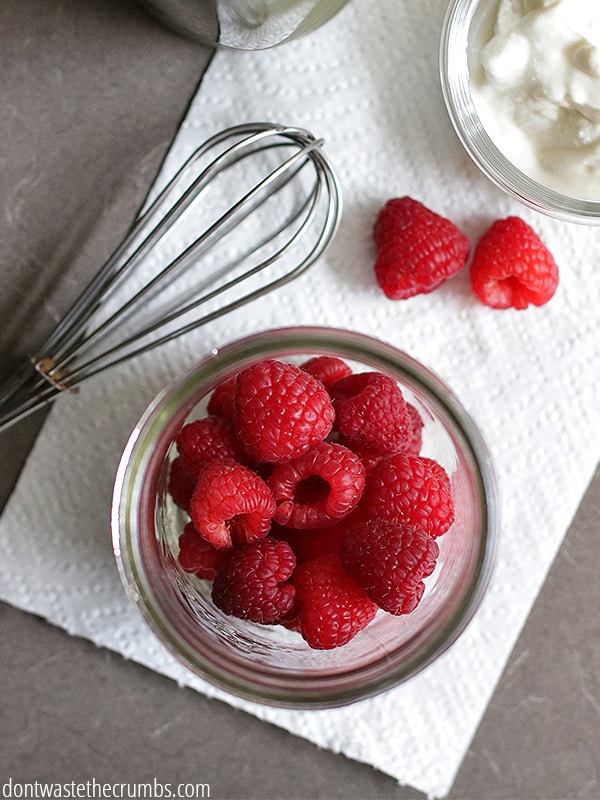 A glass jar of raspberries on a paper towel. There is a whisk next to the jar.