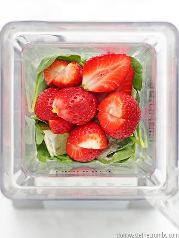 Bird's eye view of a blender full of sliced fresh strawberries and spinach leaves.