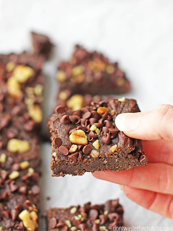 Freshly sliced black bean brownies with chocolate chips and walnuts on top. A hand holds a square slice that is ready to enjoy!