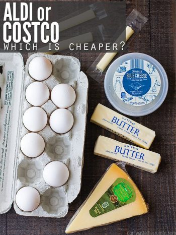 Eggs, string cheese, blue cheese carton, sticks of butter, and a wedge or parmesan on a brown background. Text overlay says "Aldi or Costco, Which Is Cheaper?"