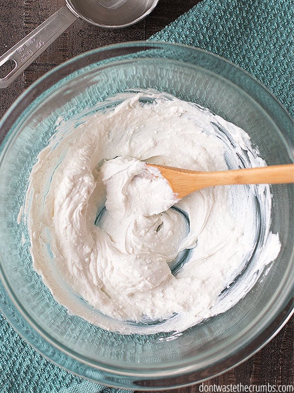 Homemade sunscreen being mixed with a wood spoon in a large glass bowl.