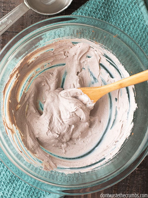 Homemade sunscreen tinted with cocoa powder being mixed with a wood spoon in a large glass bowl.