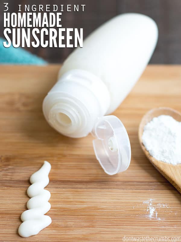 Squeezable tube with homemade sunscreen. A small amount of sunscreen is displayed on a wood cutting board with a wood spoon with white powder. Text overlay reads, "3 Ingredient Homemade Sunscreen".