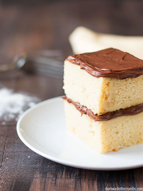 Thick layers of chocolate frosting line the center and top of this slice of yellow cake.