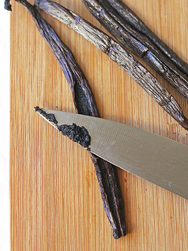 Up close view of vanilla bean on a wooden cutting board. There is a knife with a little bit of vanilla bean on it. Try making this homemade recipe today for vanilla extract!