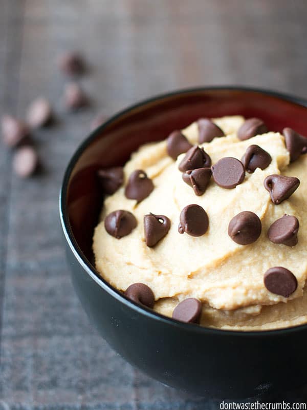 A bowl of cookie dough hummus topped with chocolate chips, with more chocolate chips scattered in the background