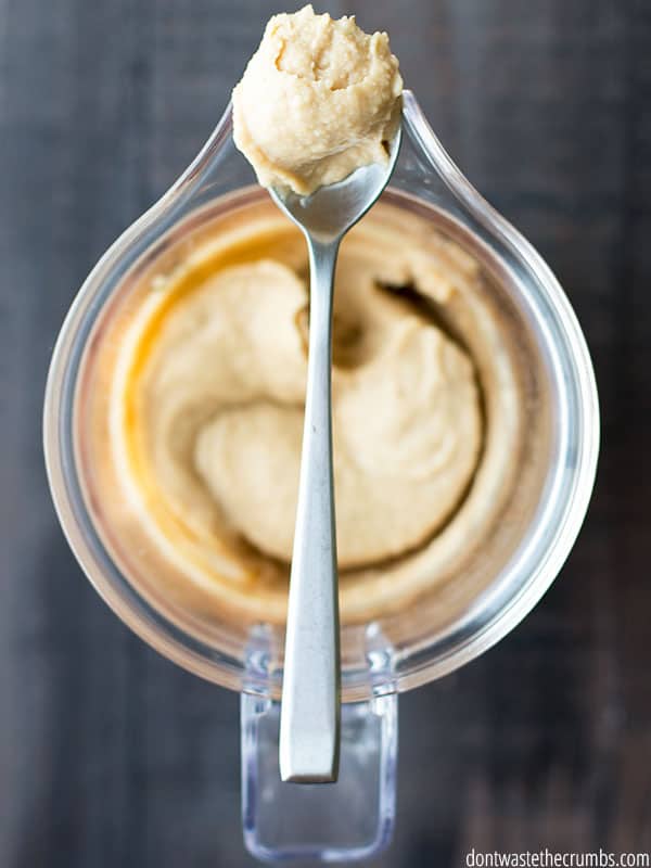 Blender of cookie dough hummus and a spoon resting on top filled with cookie dough hummus.