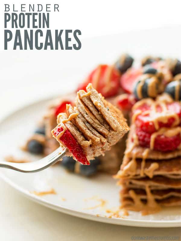 Stack of protein pancakes with fresh toppings and peanut butter drizzled on top in the background. Up close view of fork containing a bite size portion of the protein pancakes. Text overlay reads, "The Very Best Protein Pancakes".