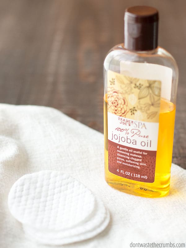 Bottle of jojoba oil and cotton pads on a paper towel