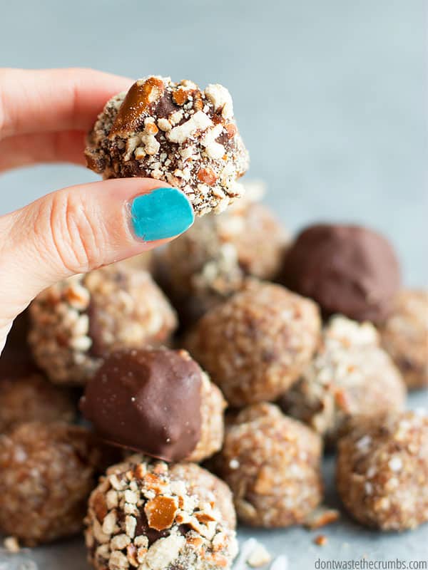 A hand holding one No Bake Sweet Salty Energy Bite, probably on it way to Tiffany's mouth. In front of a stack of delicious bite sized snacks.