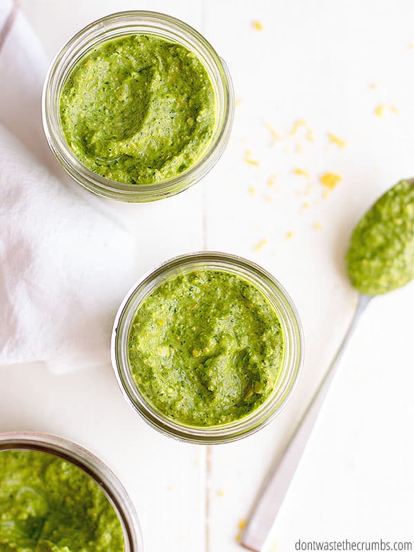 Glass jars of spinach pesto sauce and a spoonful next to a glass jar.