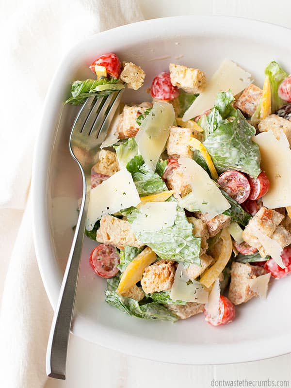 Bowl full of panzanella bread salad and salad dressing. Fork  has a bite size portion laying in the bowl.