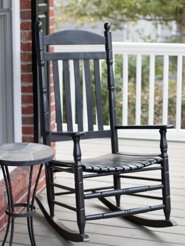 A black rocking chair and table sit on a fenced porch with white railings.