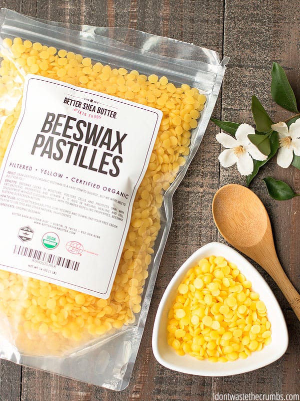 A small, measured bowl of yellow beeswax pastilles lays beside a bag of  certified organic pastilles.