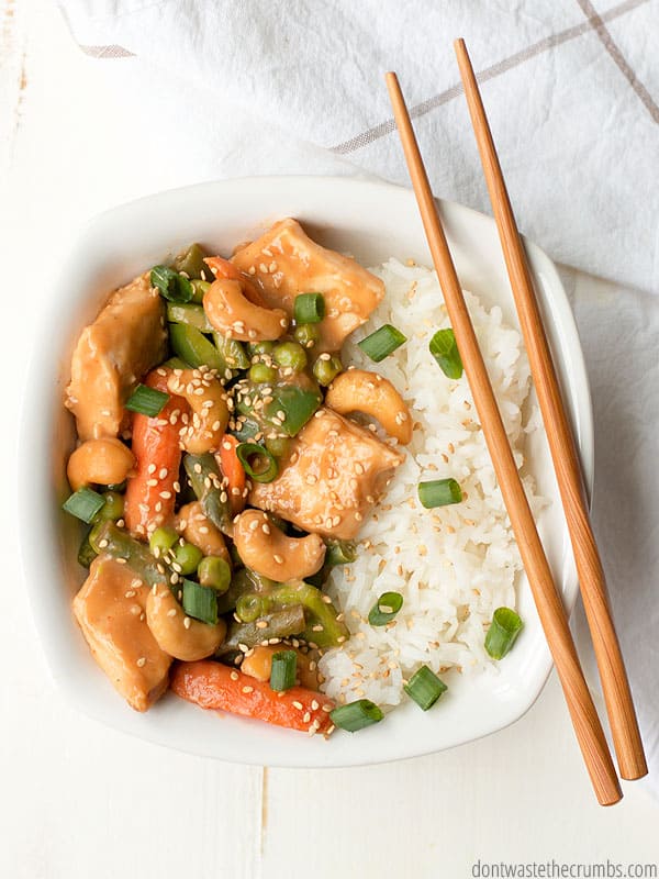 Cashew chicken over white rice in a white bowl with chopsticks.