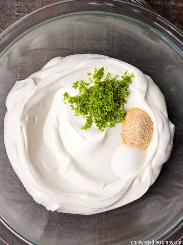 A bowl with sour cream, salt, garlic powder, and lime zest waiting to be mixed