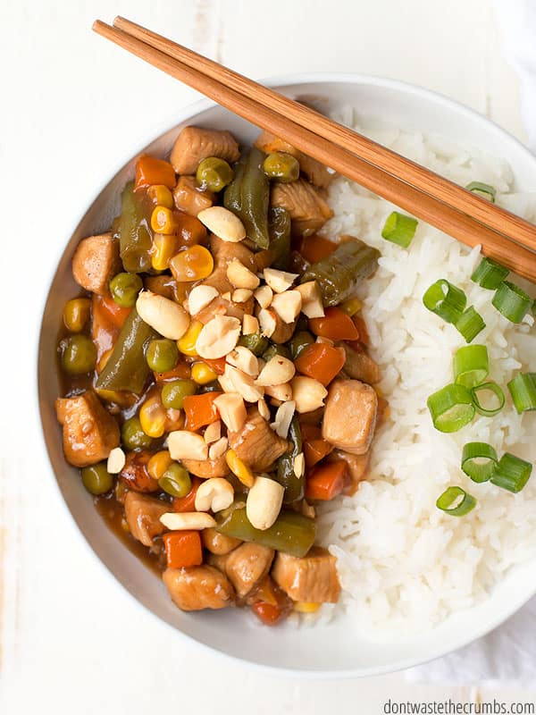 Kung Pao chicken with white rice in a white bowl. Chopsticks are laying across the bowl.