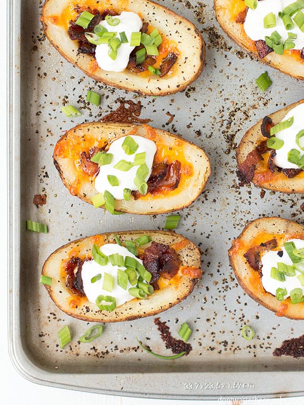 Potato skins with sour cream, bacon, cheese, and green onion on a baking sheet.