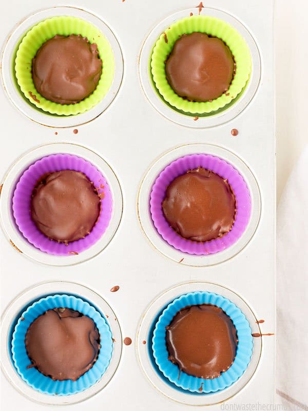 6 peanut butter cups in silicone molds sitting inside a muffin pan on top of a table.