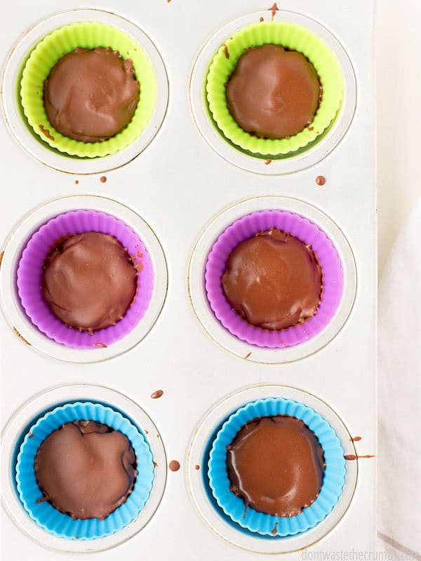 6 peanut butter cups in silicone molds sitting inside a muffin pan on top of a table. 