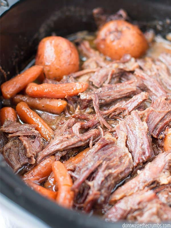 This is freshly cooked slow cooker pot roast with carrots in a black slow cooker insert.