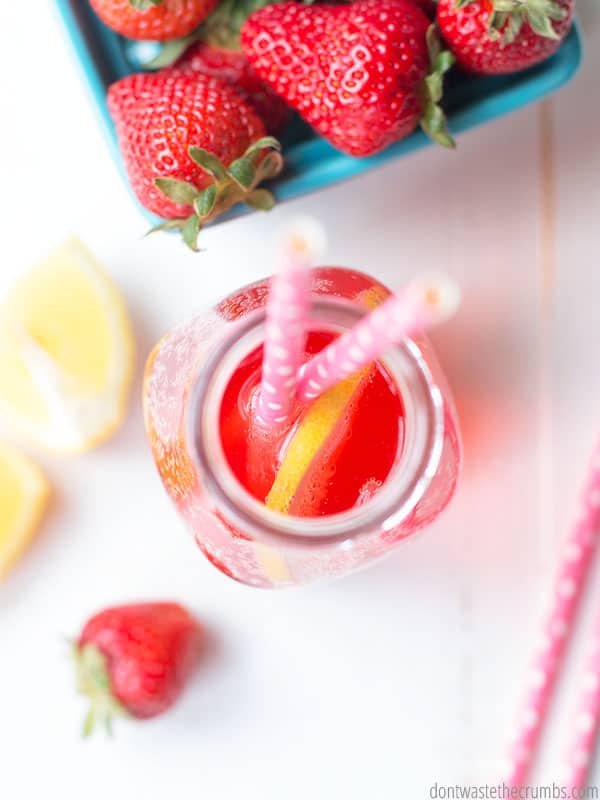 Overview of strawberry kombucha bottle with two straws in it and a slice of lemon