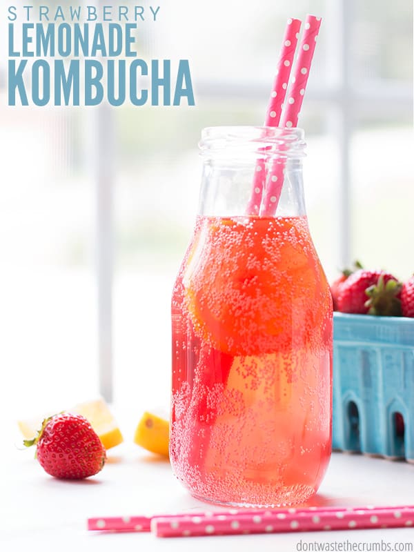 Bottle of strawberry lemonade kombucha with strawberries in a basket. Text overlay says, "Strawberry Lemonade Kombucha".