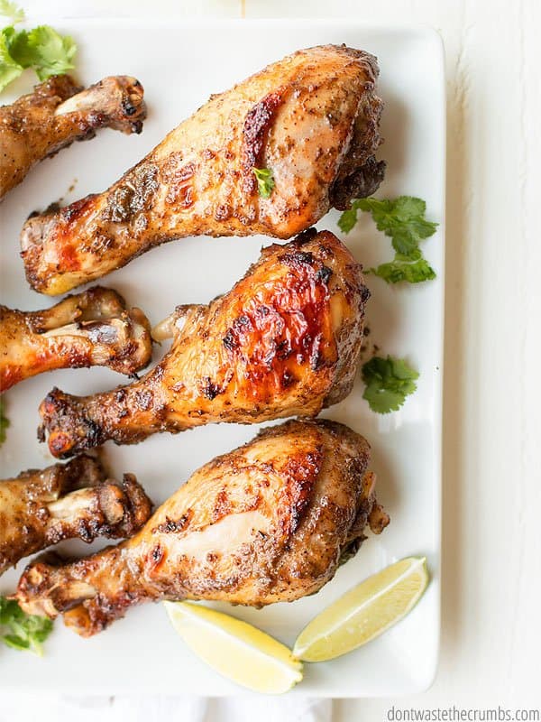 Overview shot of 6 jerk chicken drumsticks on a white plate and some cilantro on the plate and two slices of lemon