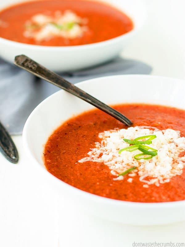 Roasted red pepper tomato soup with a sprinkle of cheese in a white bowl.